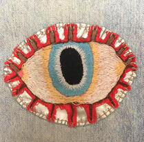 a hand-embroidered eye, with a blue iris and red eyelashes.